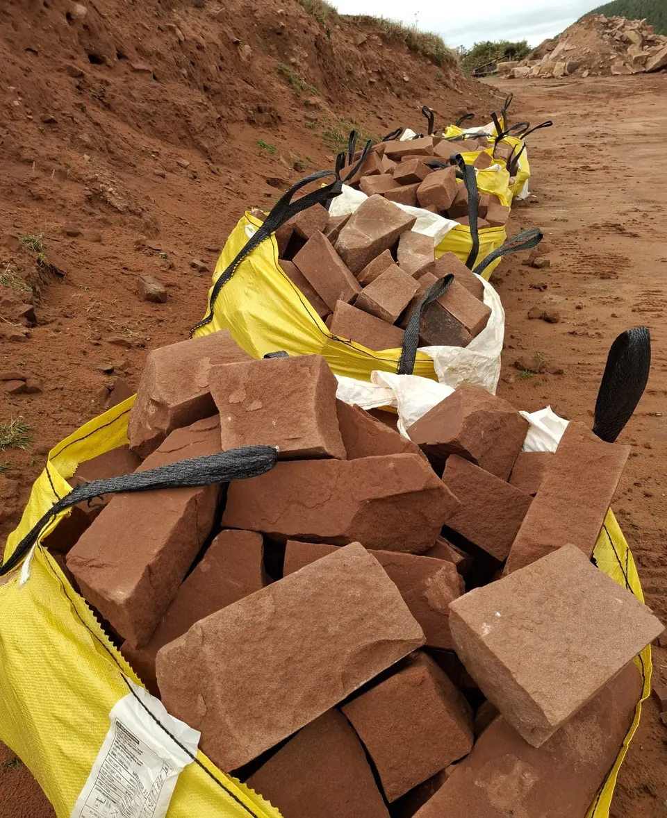 A line of yellow bulk bags filled with red sandstone on the quarry bank