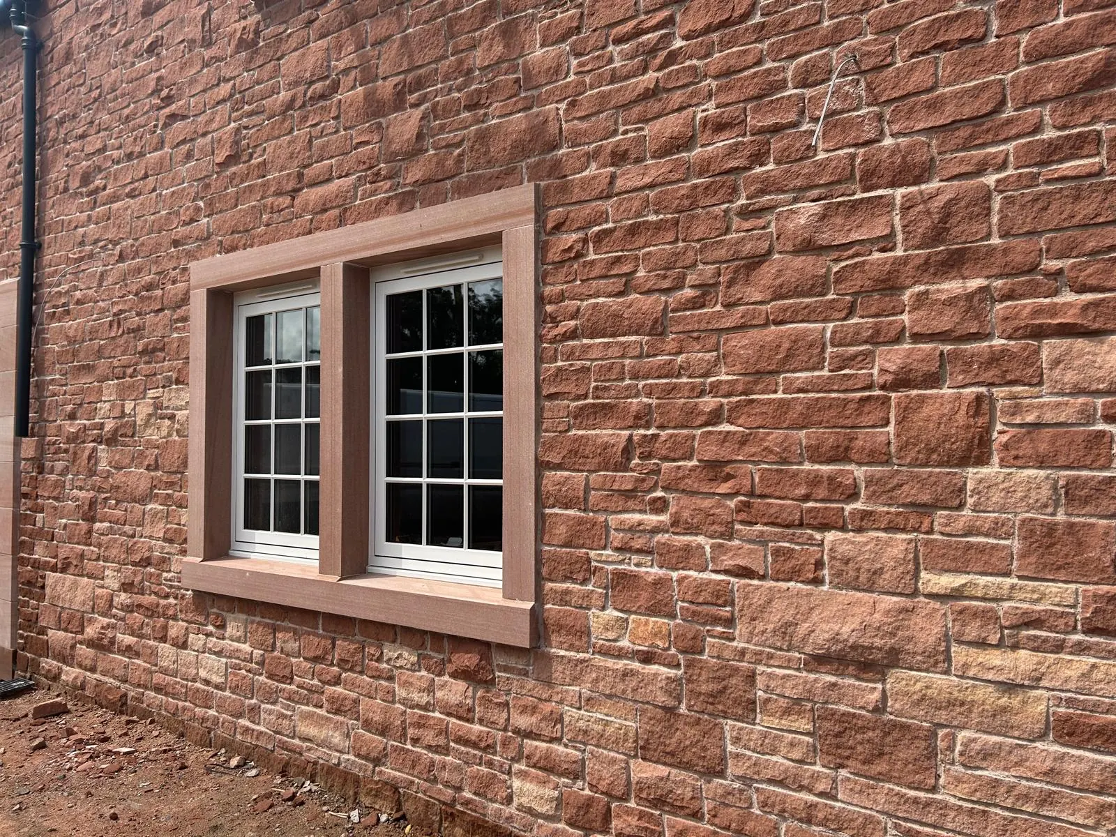 A finished house elevation in red sandstone with paired white sash windows and dressed stone surrounds