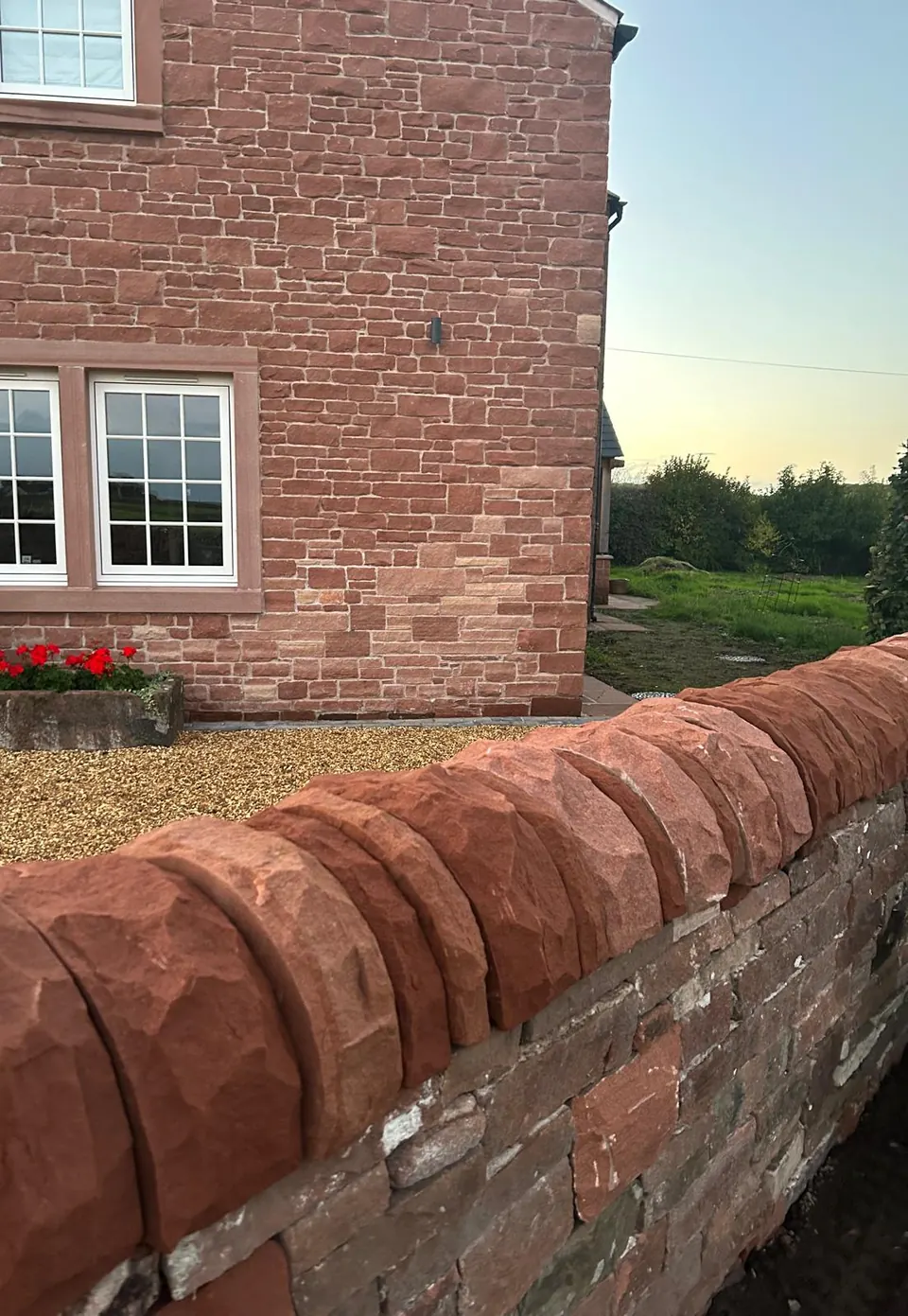 Rock-faced red sandstone copes on a garden wall in front of a house