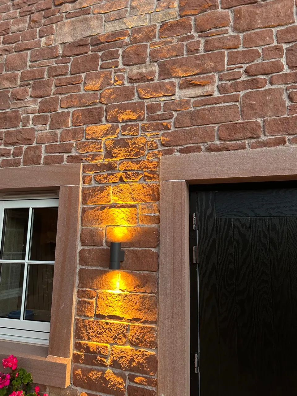 Close-up of red sandstone wall lit by an amber wall light beside a dressed door surround