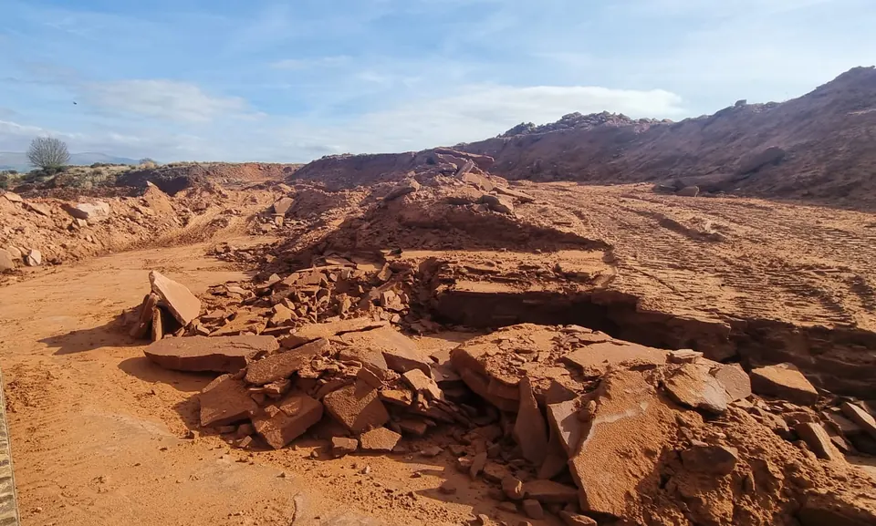 An excavator working the red sandstone quarry floor under a blue sky